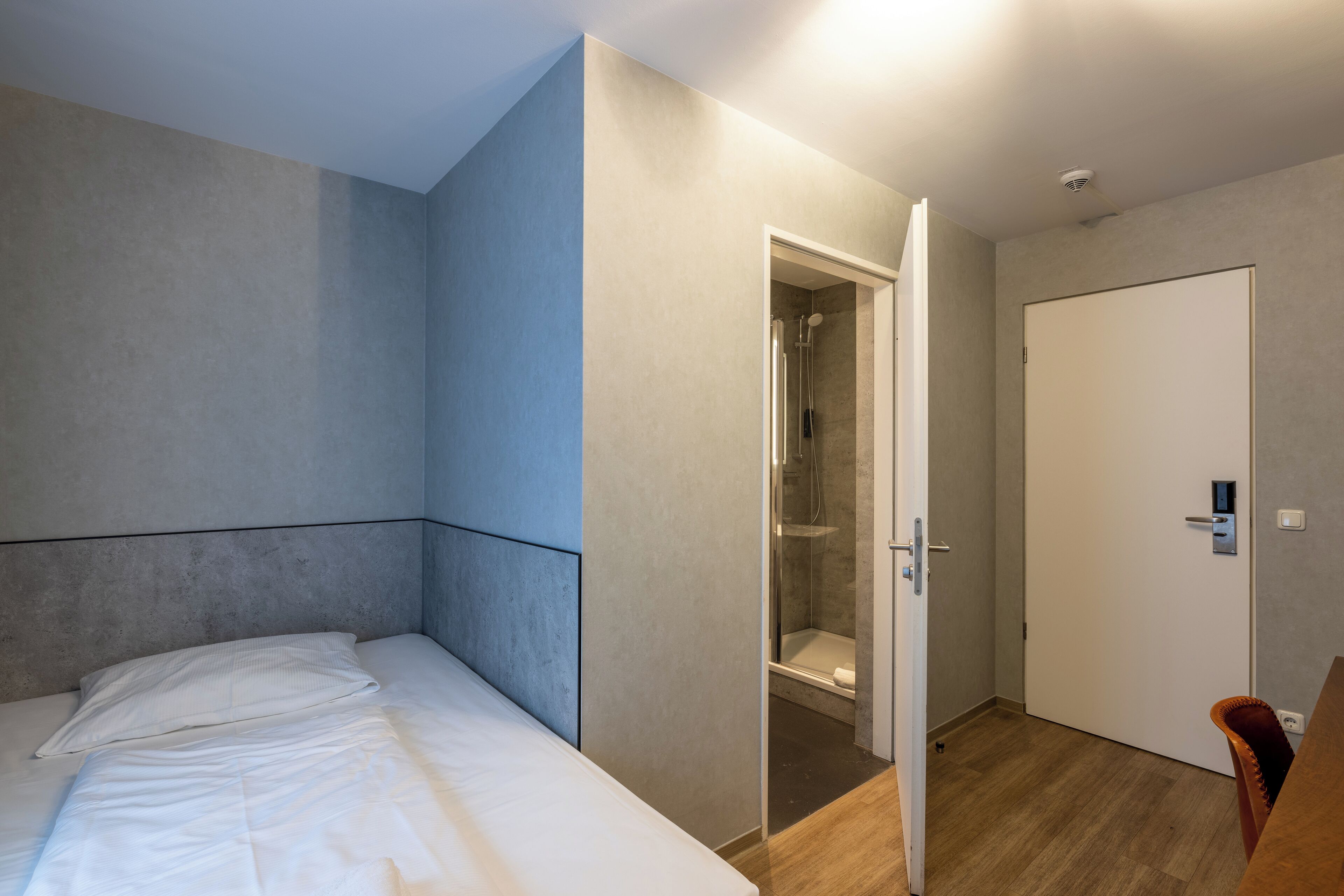 A modern hotel room with a bed, a shower area, and a door.