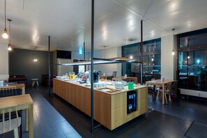 A modern cafe with a central counter, seating area, and large windows. - mk | hotel stuttgart (Stuttgart)