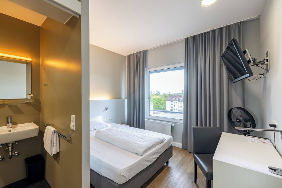 Et hotelværelse med seng, natbord, skrivebord og et vindue med gardiner.