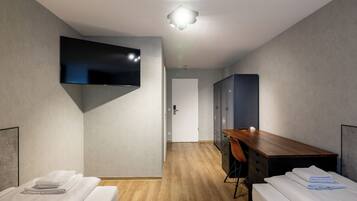 A hotel room with two beds, a wooden desk, a flat-screen TV mounted on the wall, and a wardrobe.