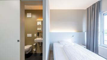 A hotel room with a bed, a bathroom with a toilet and sink, and a window with curtains.