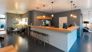 A modern hotel lobby with a reception desk, bar stools, seating area, and a coffee machine. - mk | hotel stuttgart (Stuttgart)