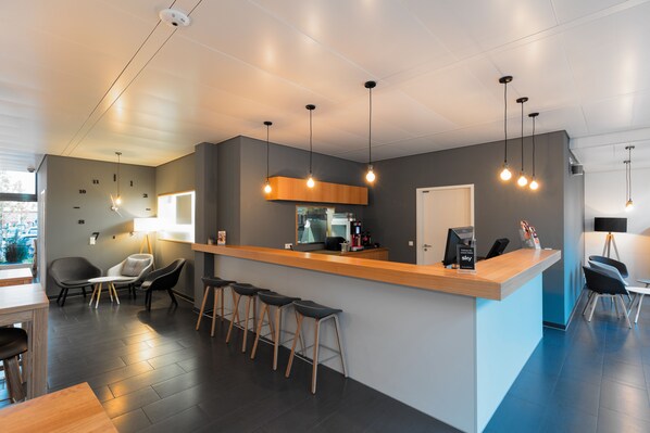 A modern hotel lobby with a reception desk, bar stools, seating area, and a coffee machine. - mk | hotel stuttgart (Stuttgart)