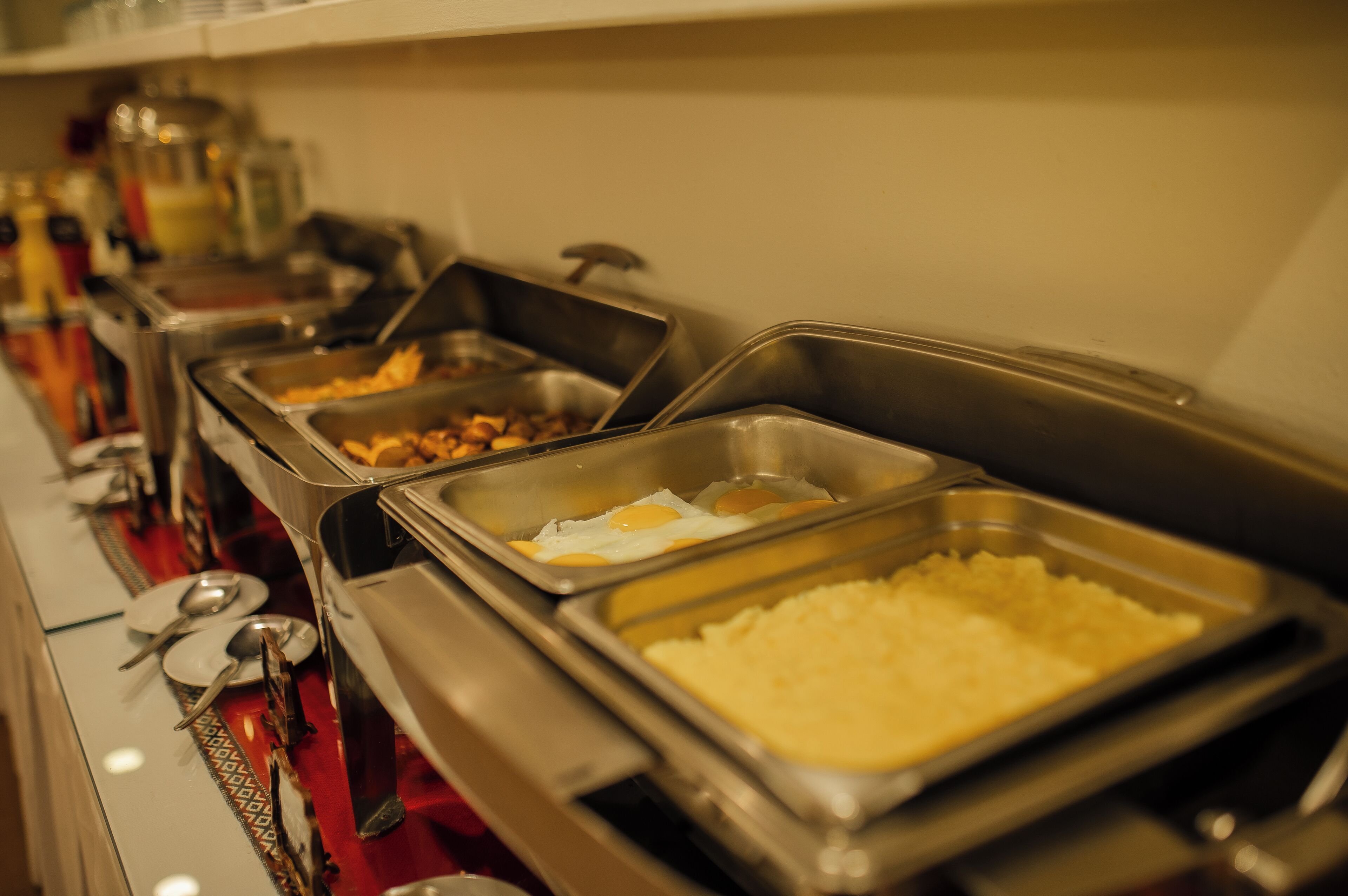 A buffet with various food items including eggs, potatoes, and other dishes in metal serving trays.