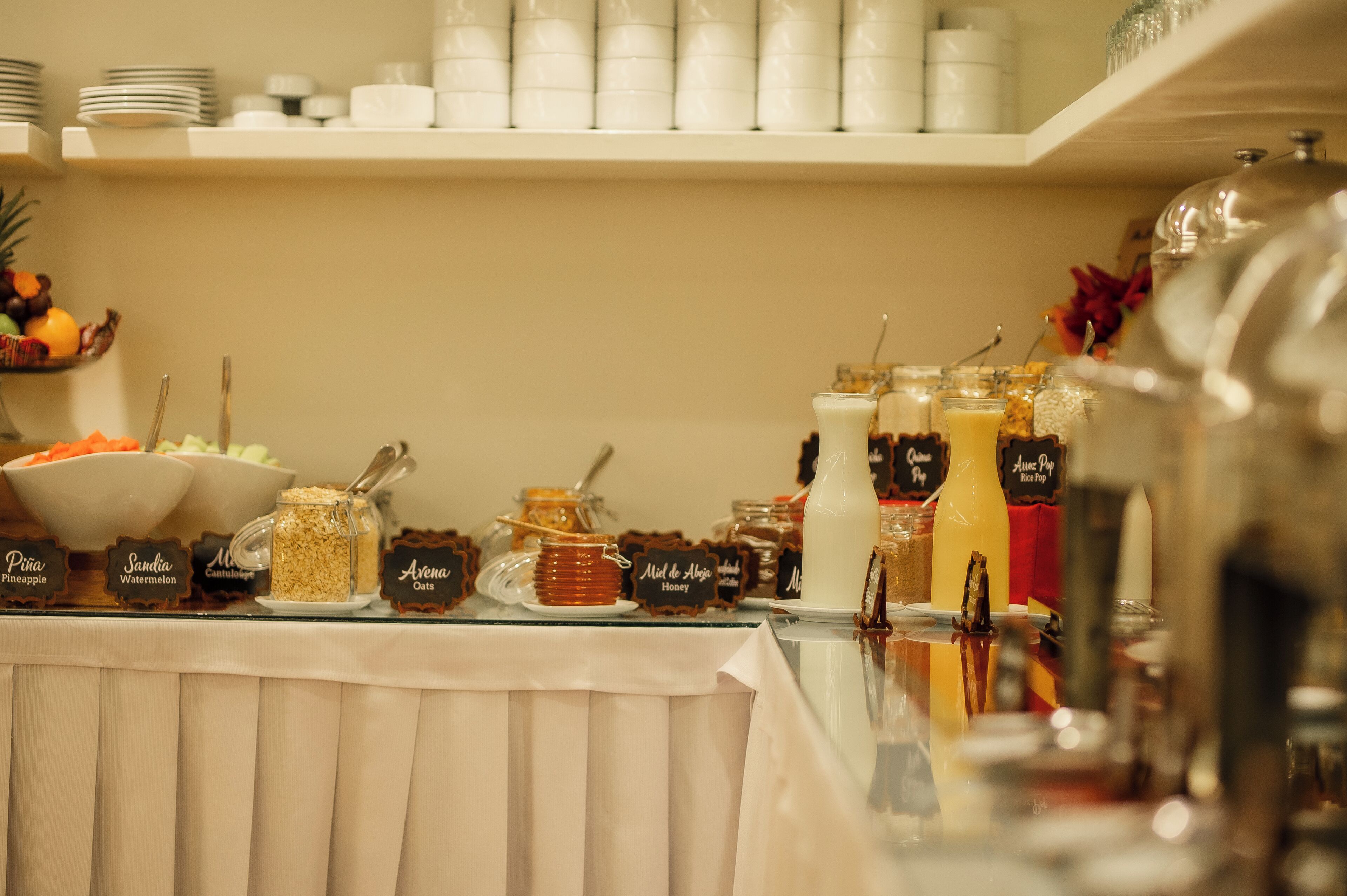 A buffet table with various food items and drinks, including jars of oatmeal, honey, and a large bottle of milk.