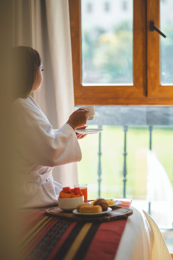 Una persona vestida de blanco sentada junto a una ventana con una bandeja de desayuno.