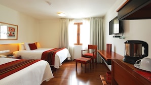 Habitación de hotel con dos camas, televisor, cafetera y ventana con cortinas.