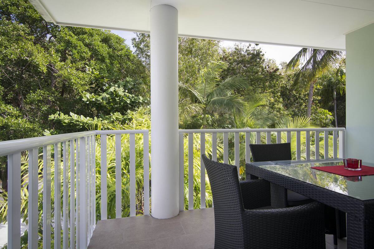 A balcony with a white railing, a glass table, wicker chairs, and a red candle holder.