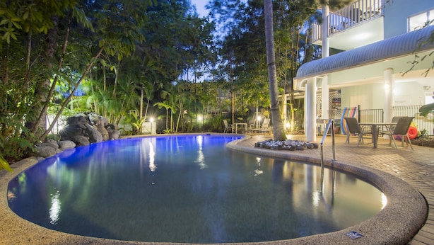 Uma piscina rodeada por pedras e árvores, com um edifício ao fundo.
