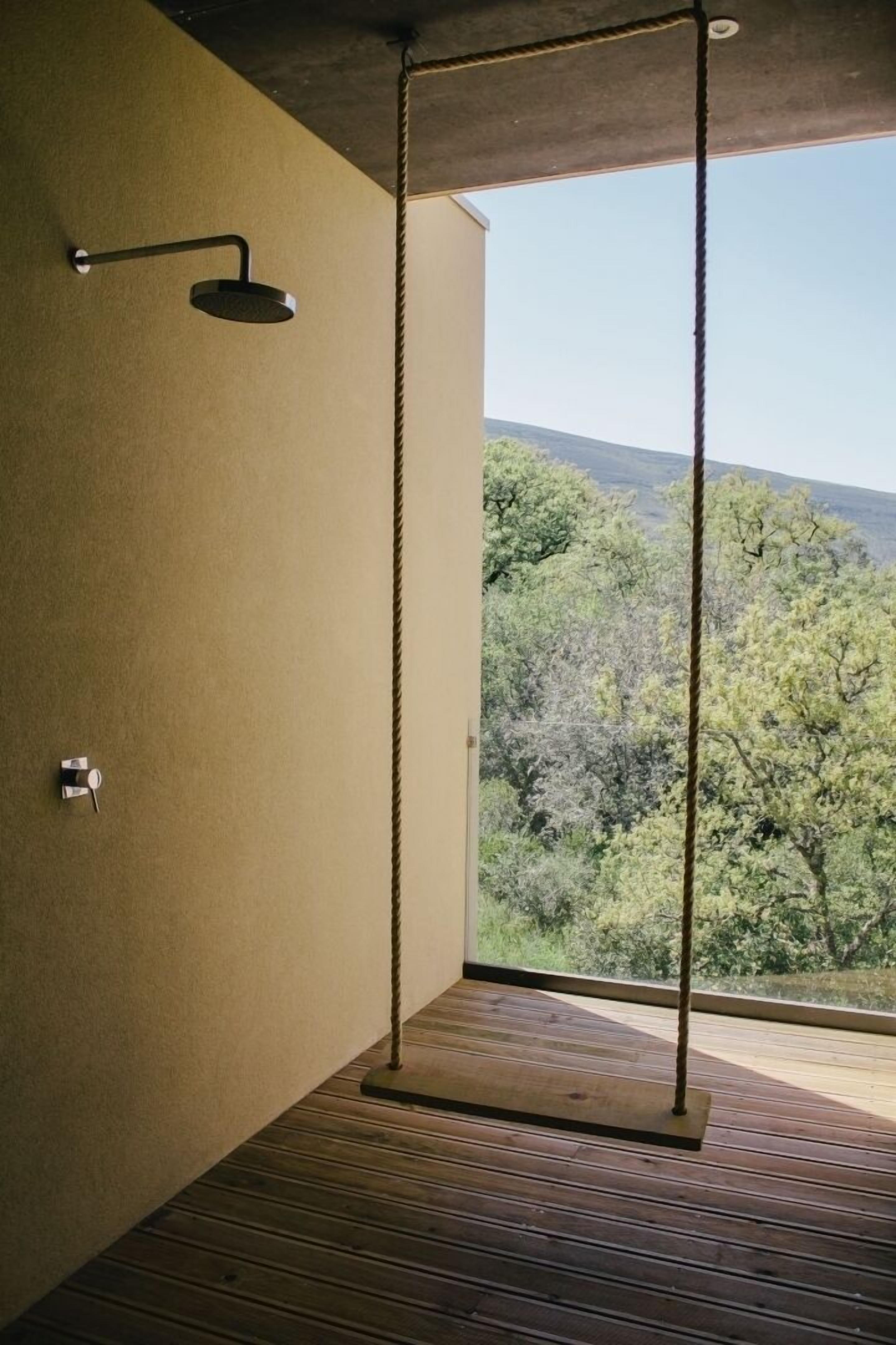 Ducha moderna con tirador de cuerda, suelo de madera y vista a árboles a través de un ventanal grande.