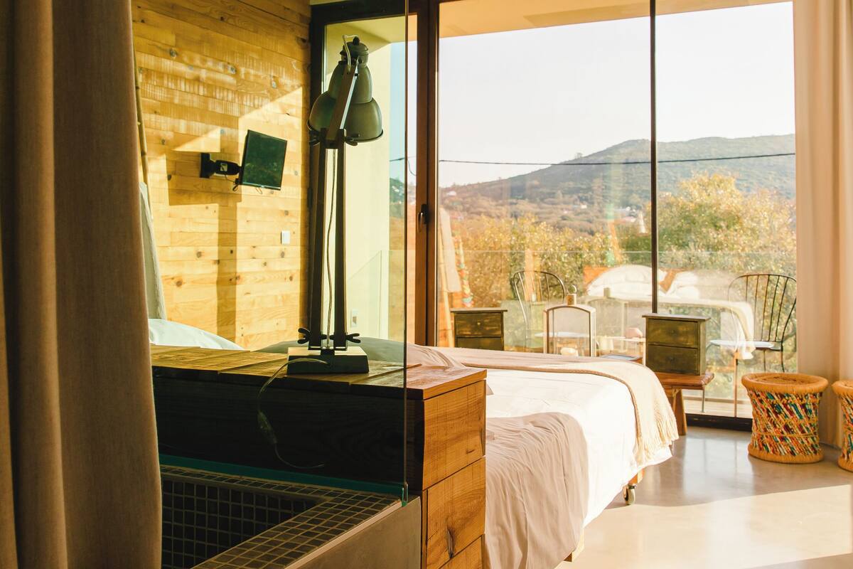 Une chambre avec une grande fenêtre, un lit, un bureau et une chaise.