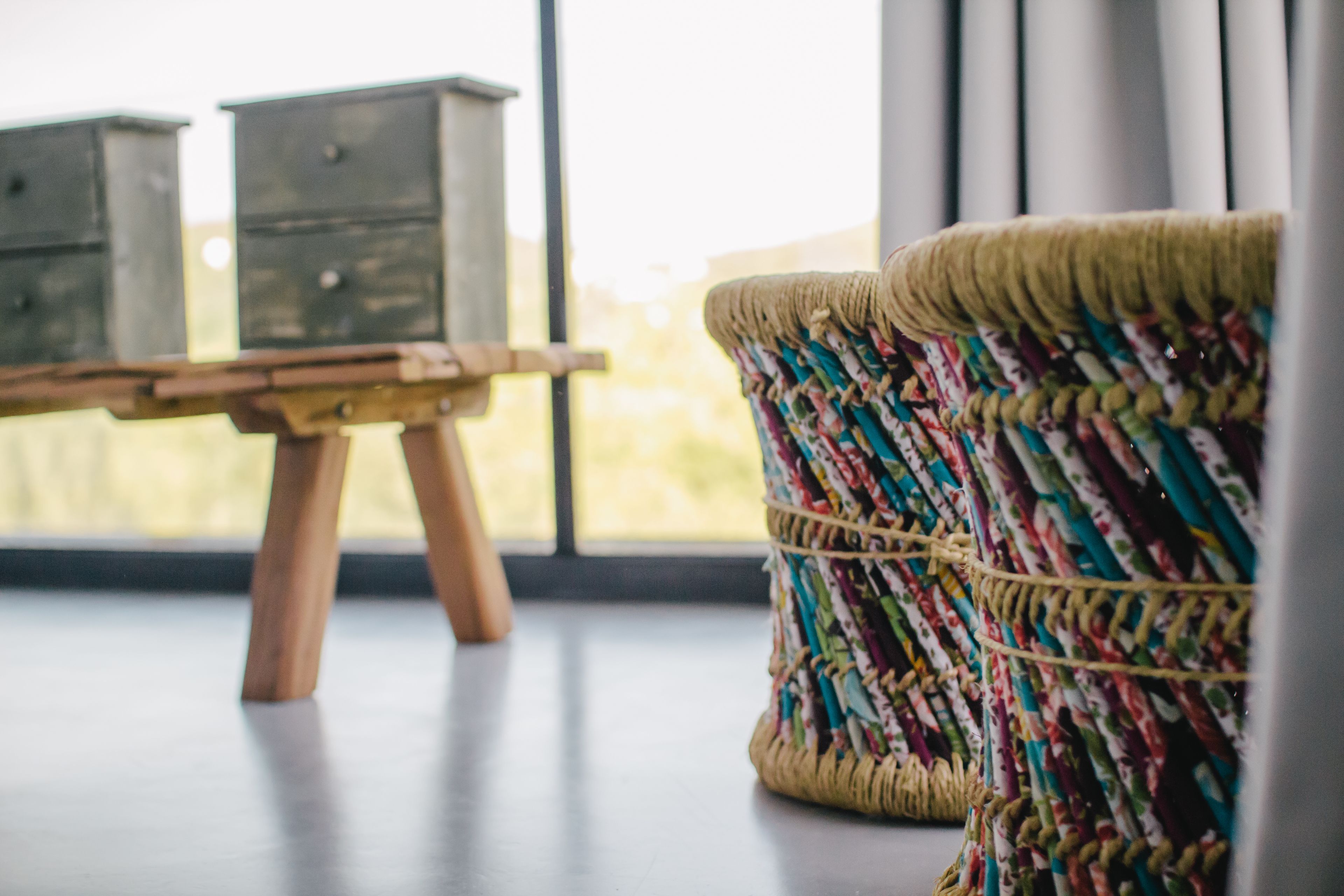 Een kamer met een houten tafel, twee opbergkasten en een kleurrijk geweven pouf.