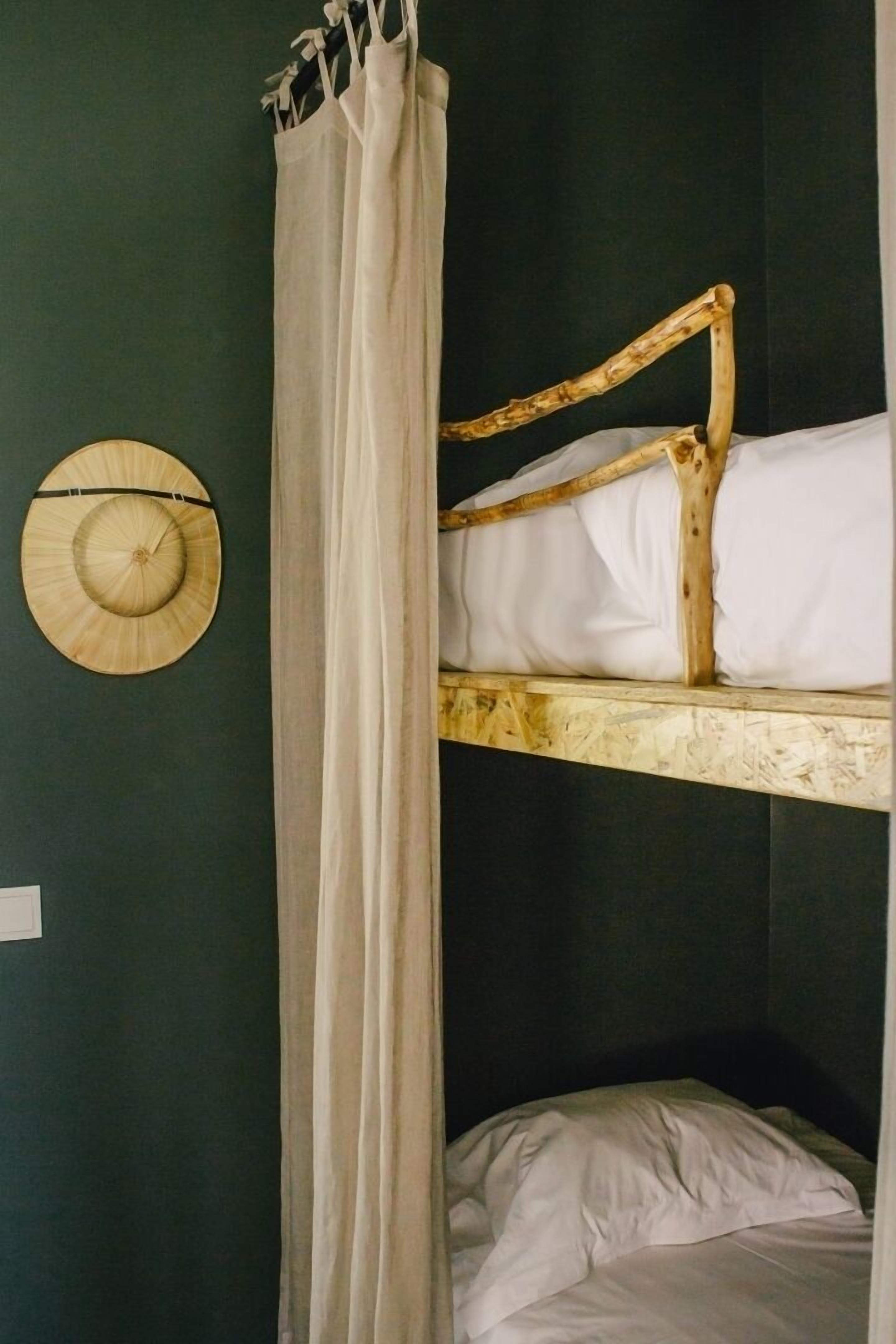 Ein Stockbett mit Holzrahmen, weißer Bettwäsche, einem Vorhang und einem an der Wand befestigten Ventilator.