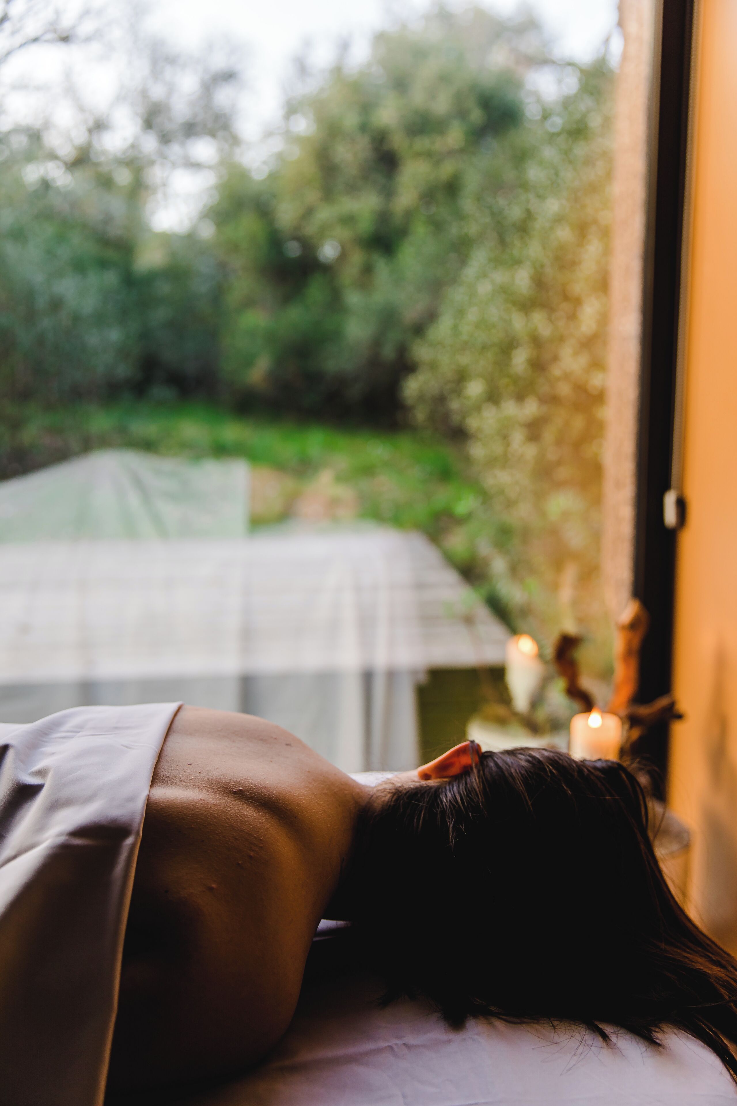 A person lying on a bed with a view of a garden outside.