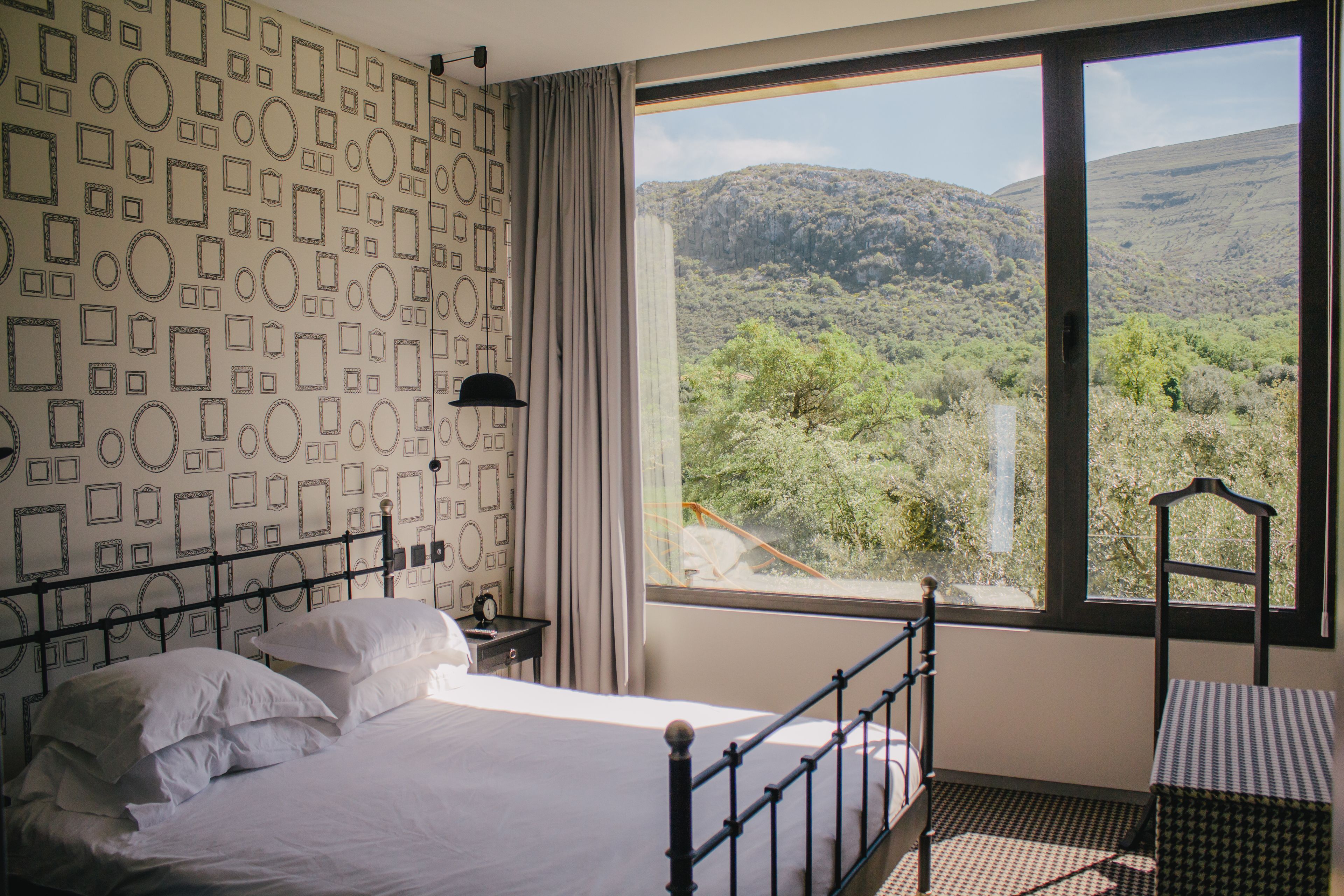 A bedroom with a bed, a nightstand, a window with a mountain view, and a patterned wall.