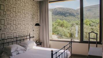 A bedroom with a bed, a nightstand, a window with a mountain view, and a patterned wall.