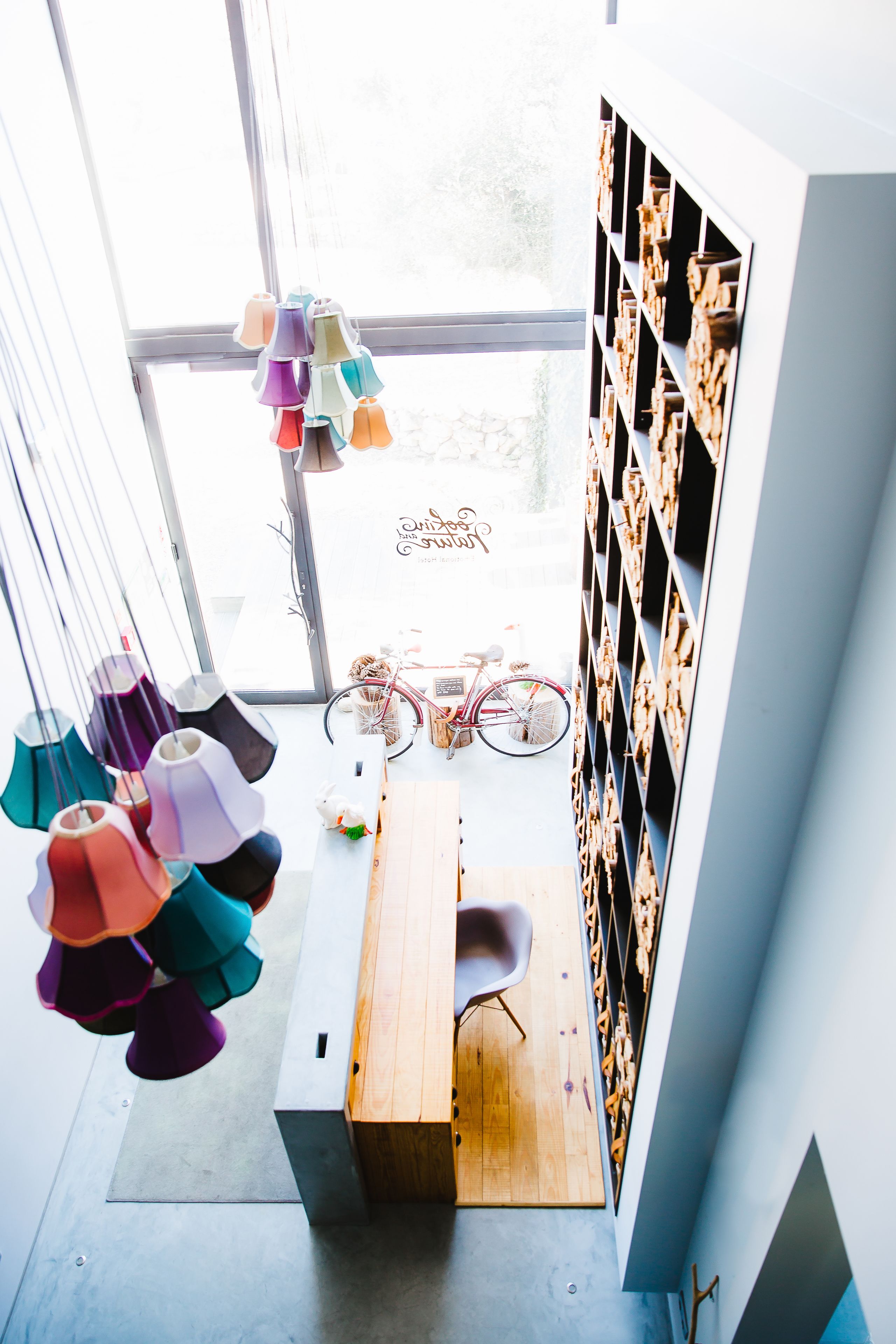 A room with a wooden desk, colorful hanging lamps, a bicycle, and a wall with shelves of decorative items.