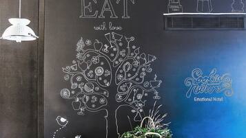 Un coin repas avec un mur noir orné d’un dessin d’arbre et des mots « MANGEZ avec amour ». On y voit un vélo avec un panier portant l’inscription « SENS », et une cheminée en arrière-plan.