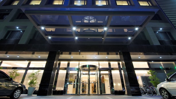 A modern hotel entrance with a revolving door, glass facade, and a parking area with cars and bicycles. - Guanko Hotel (Chiayi City)