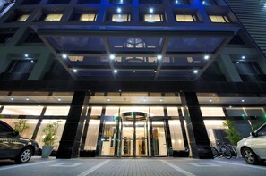 L’entrée d’un hôtel moderne, dotée d’une porte tournante, d’une façade en verre et d’un espace de stationnement pour voitures et vélos.