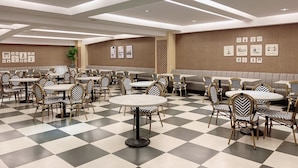 A spacious dining area with checkered flooring, round tables, and chairs with patterned upholstery. - Guanko Hotel (Chiayi City)