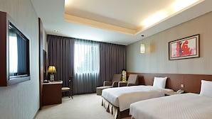 A hotel room with two beds, a desk, a chair, a TV, and a window with curtains. - Guanko Hotel (Chiayi City)