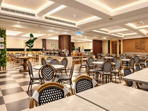 Un comedor amplio con varias mesas y sillas, una barra central y una pared decorativa.