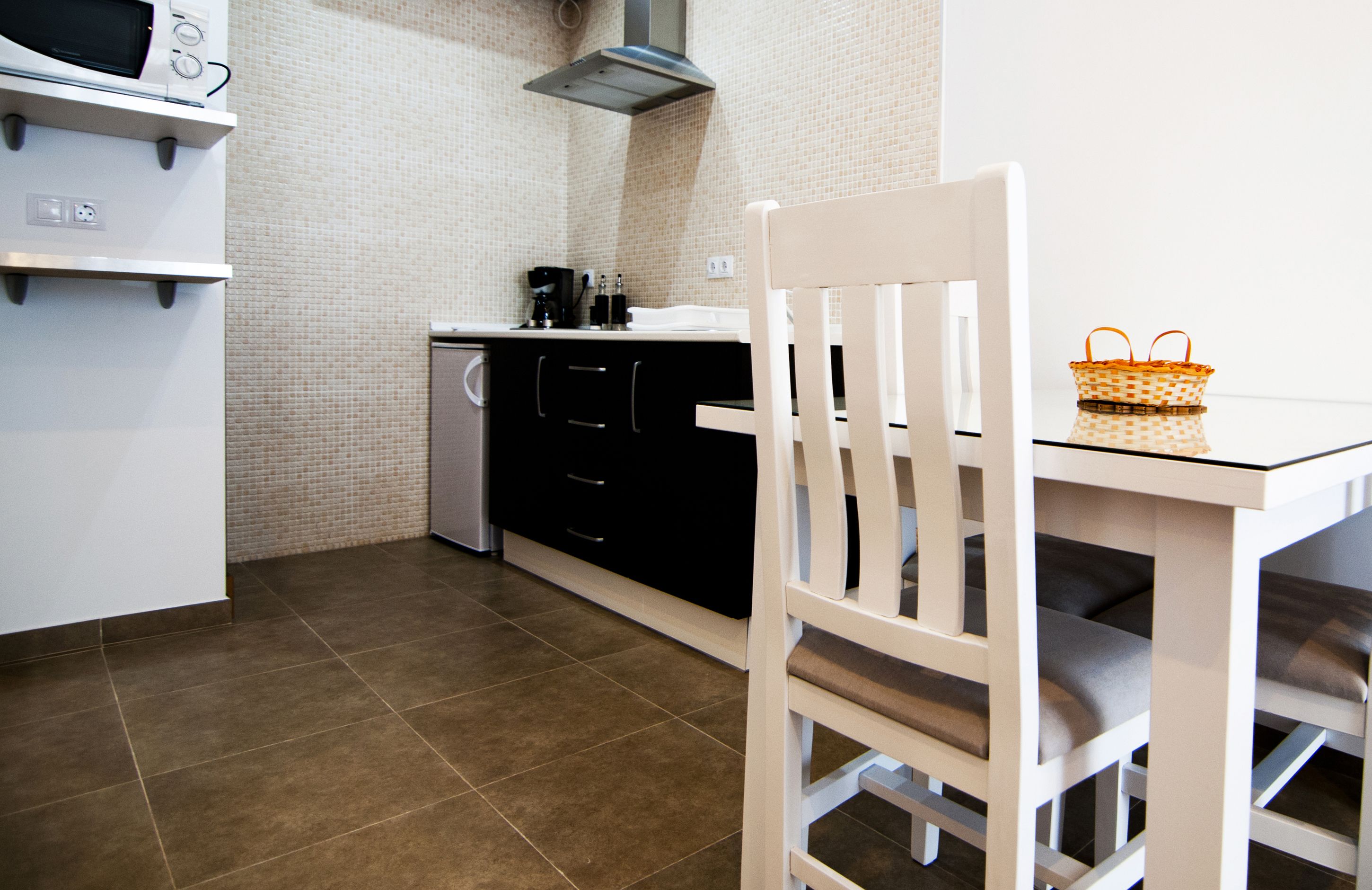 A kitchen with a microwave, stove, and sink. There is a white chair and a table with a basket.