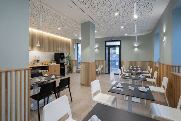 Un comedor moderno con mesas y sillas, una cocina al fondo y un techo con un diseño único.