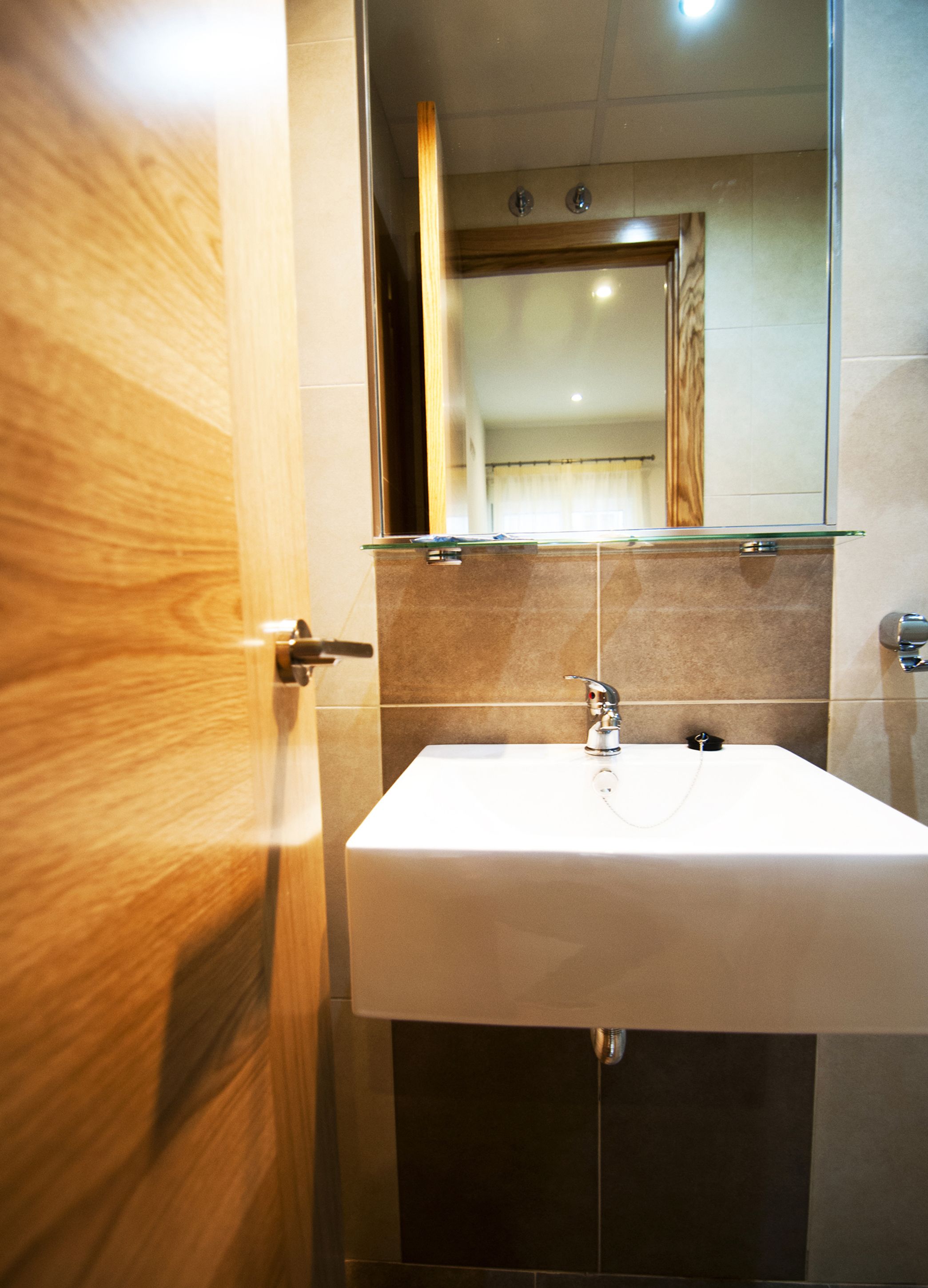 Un baño con puerta de madera, un lavamanos blanco y un espejo encima.
