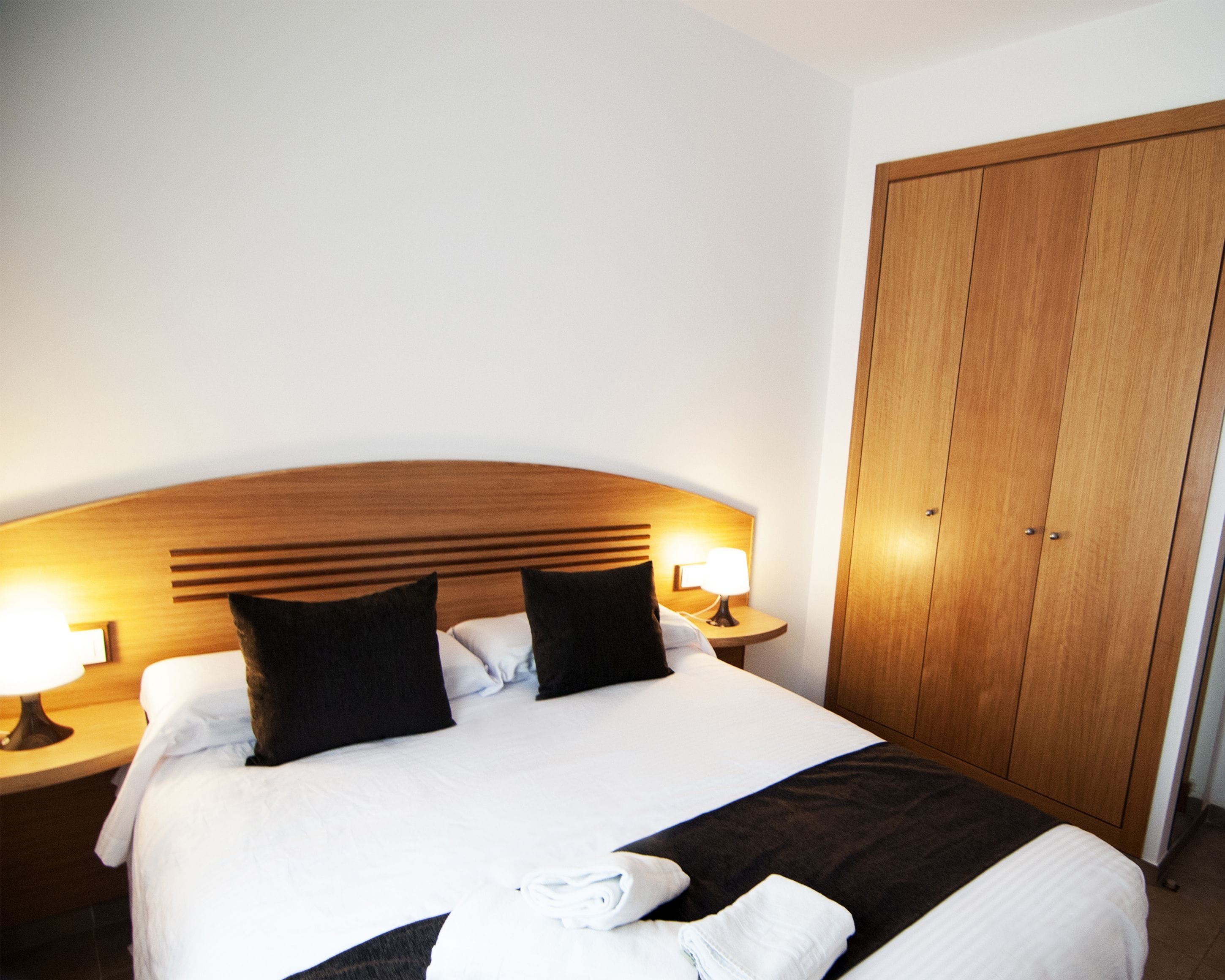 Une chambre d’hôtel avec un grand lit, deux lampes de chevet, une tête de lit en bois et une armoire.
