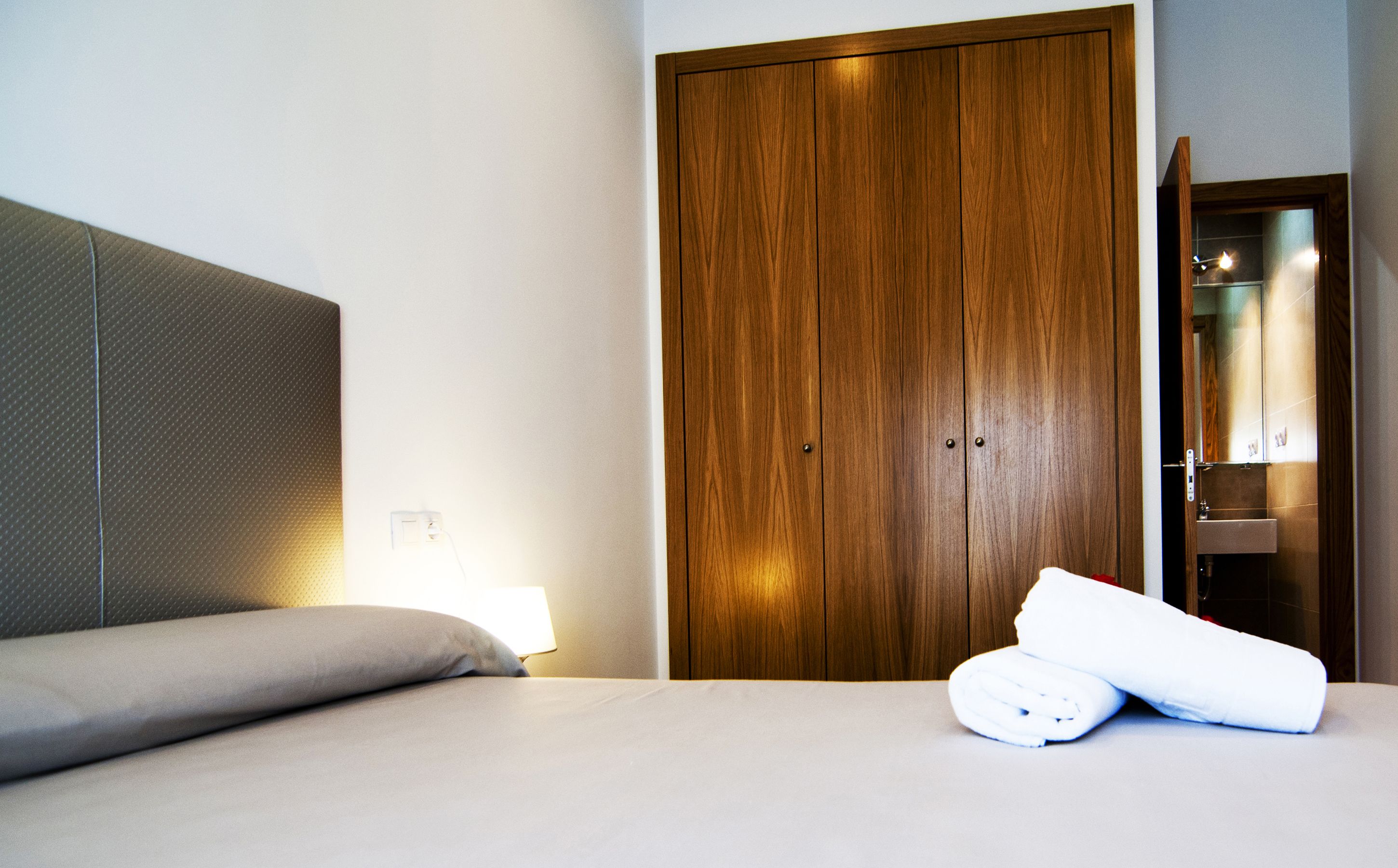 Una habitación de hotel con cama, un armario de madera y un baño con espejo y lavamanos.