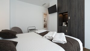 Une chambre d’hôtel moderne dotée d’un grand lit, d’un téléviseur à écran plat fixé au mur et d’une étagère intégrée où sont rangés les articles de toilette.