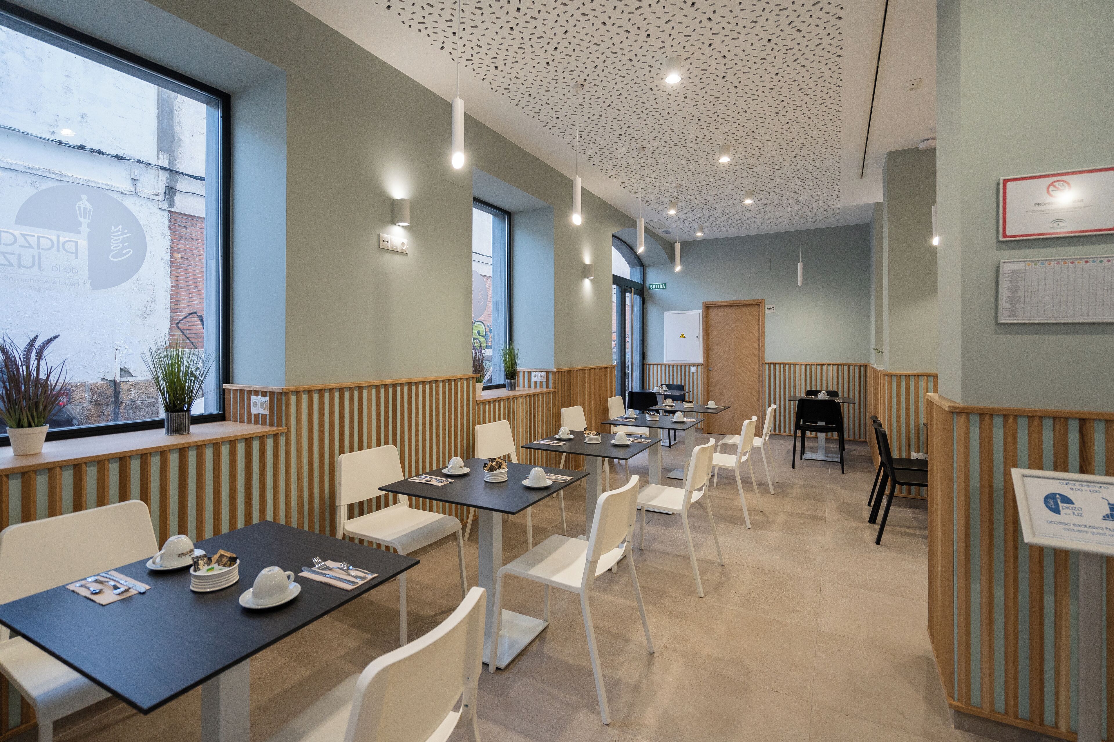 Un comedor moderno con mesas y sillas, una recepción y un amplio ventanal con vistas al exterior.