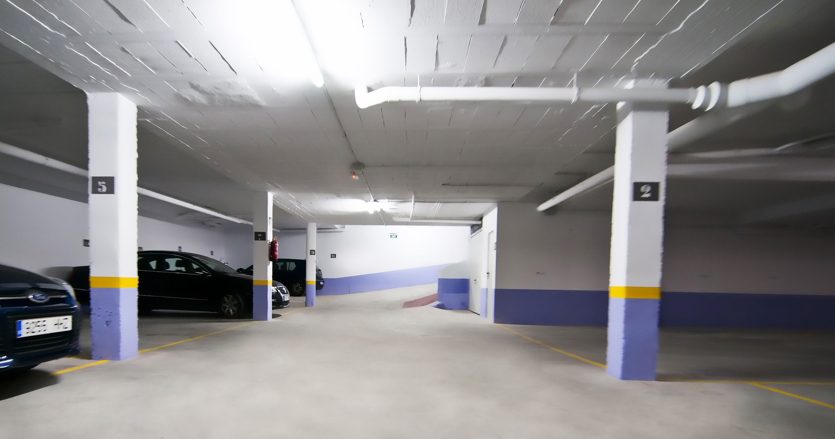 An indoor parking garage with white and blue walls, concrete pillars, and a clean, well-lit environment.