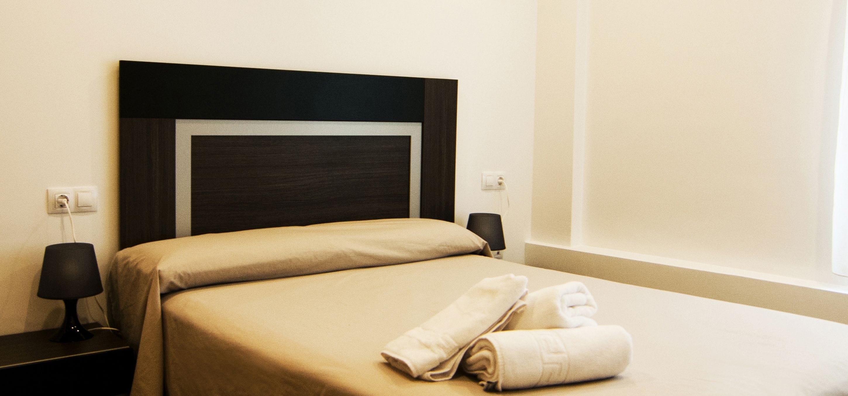 Habitación de hotel con una cama, una mesita de noche, una lámpara y una ventana.