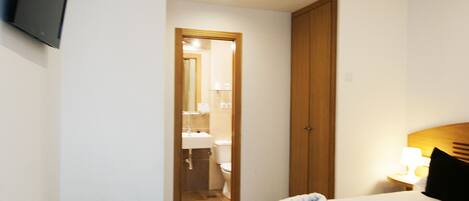 Habitación de hotel con cama, escritorio, silla, televisor montado en la pared y baño visible a través de una puerta abierta.