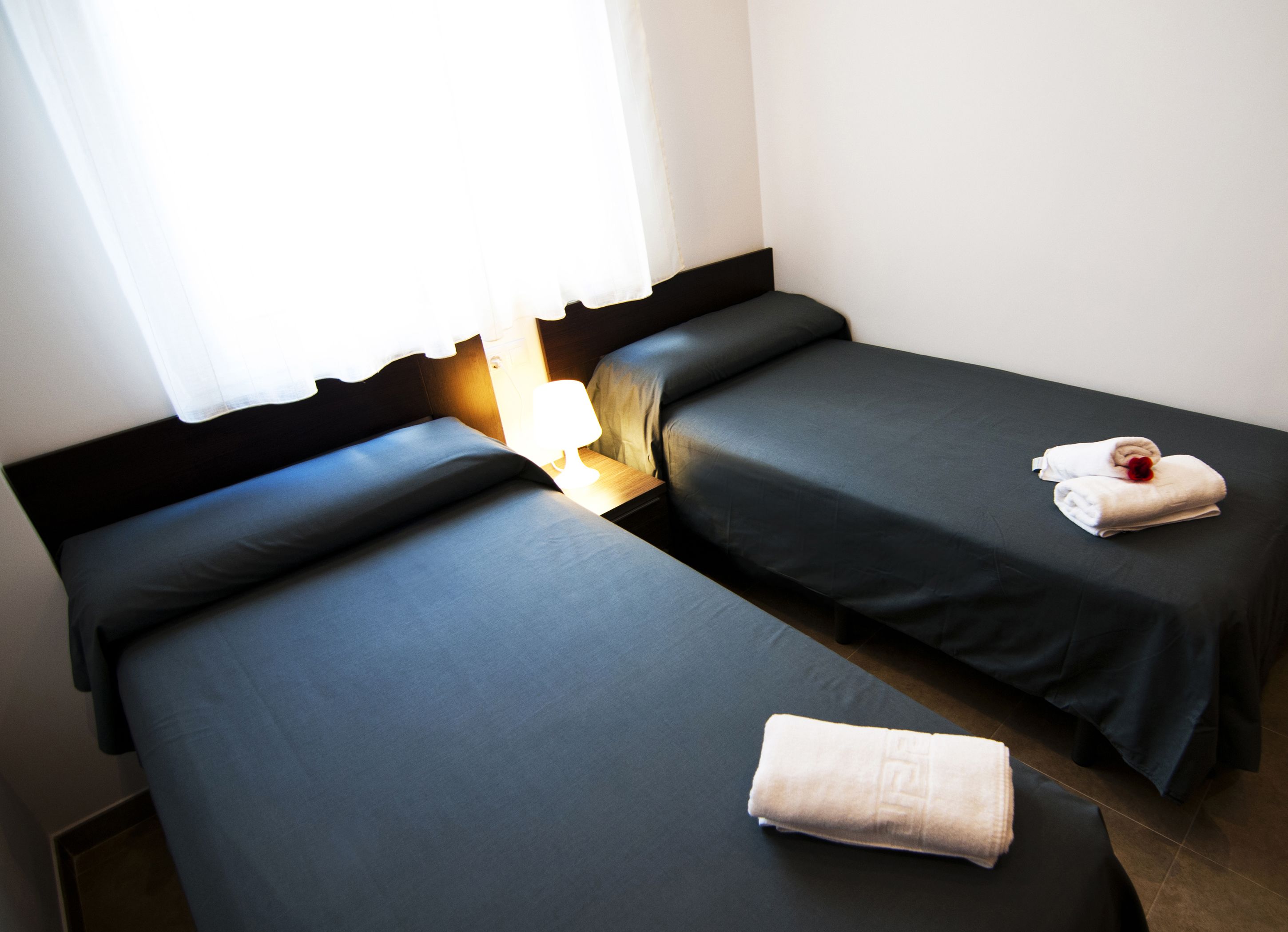Une chambre d’hôtel avec deux lits simples, une table de chevet avec une lampe et une fenêtre avec des rideaux.