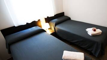 A hotel room with two single beds, a nightstand with a lamp, and a window with curtains.