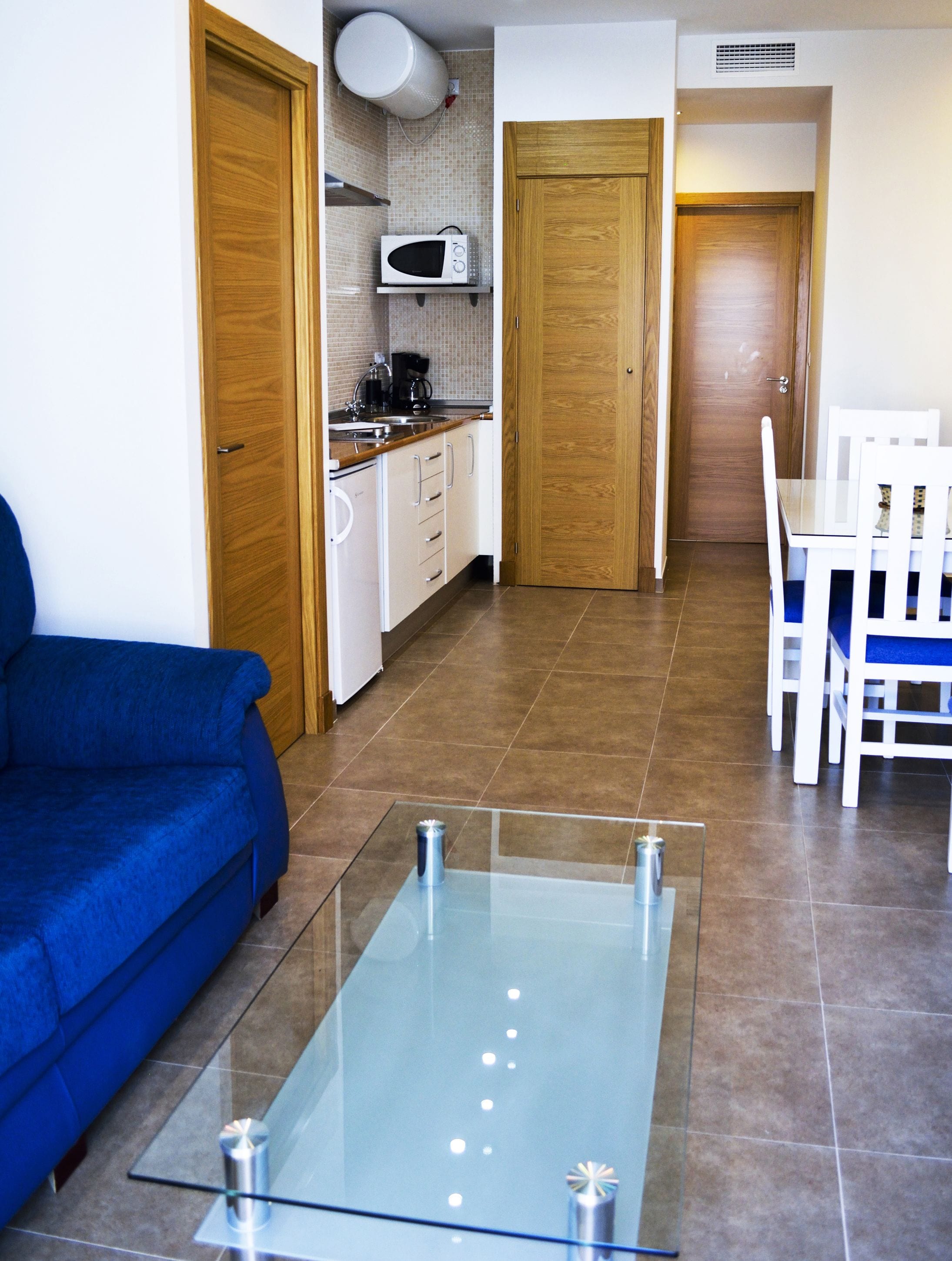 Un espacio habitable compacto con kitchenette, comedor y zona de estar con una mesa de centro de vidrio.