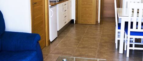 Un espacio habitable compacto con kitchenette, comedor y zona de estar con una mesa de centro de vidrio.