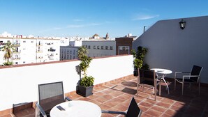 Une terrasse sur le toit, avec une table et des chaises blanches, des plantes en pot et une vue sur le paysage urbain.