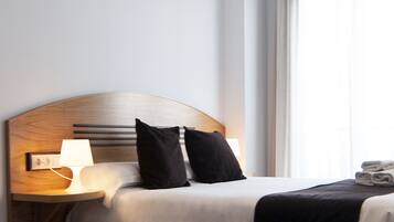 Habitación de hotel con cabecera de madera, dos almohadas negras, cubrecama blanco, lámpara de noche y ventana con cortinas.