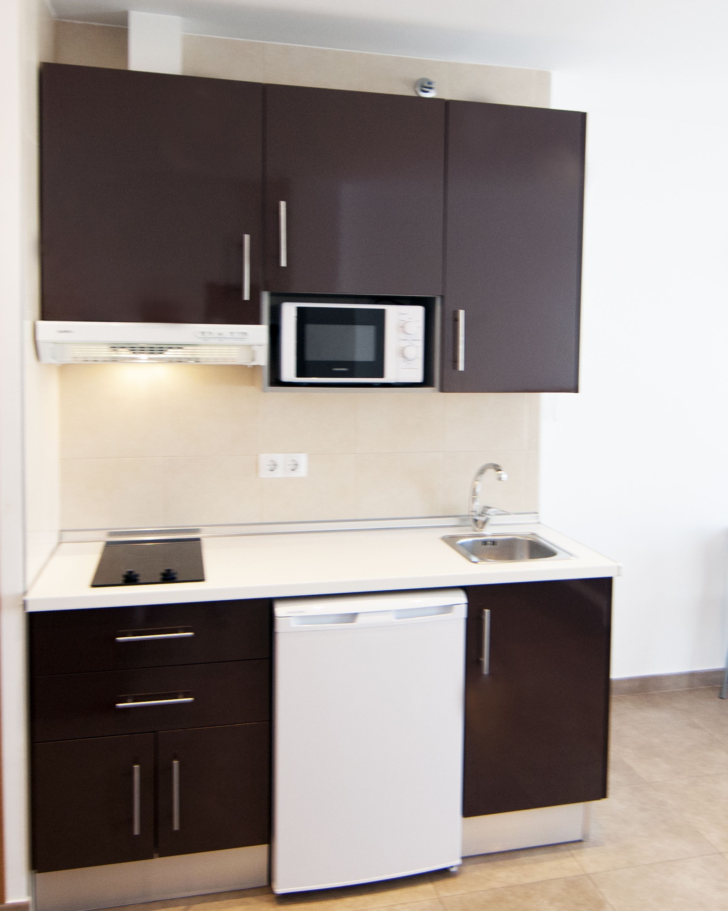 Una cocina compacta con armarios marrón oscuro, un lavavajillas blanco, un microondas y un lavabo.
