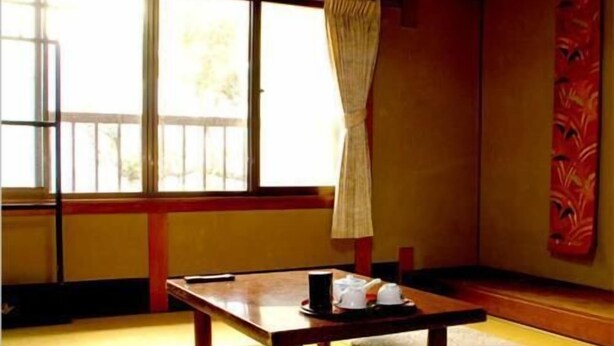 A traditional Japanese room with tatami flooring, a low table with cushions, and a window with a curtain. - Daiya Ryokan (Kyoto)