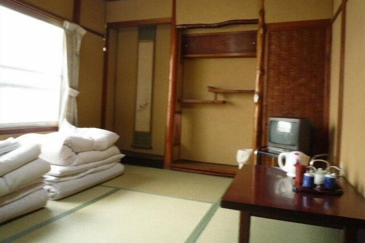 A traditional Japanese room with tatami flooring, a wooden wardrobe, a television, and a table with a teapot and cups.