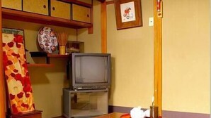 A traditional Japanese room with tatami flooring, a low table with a remote control, a television on a stand, and a decorative vase. - Daiya Ryokan (Kyoto)