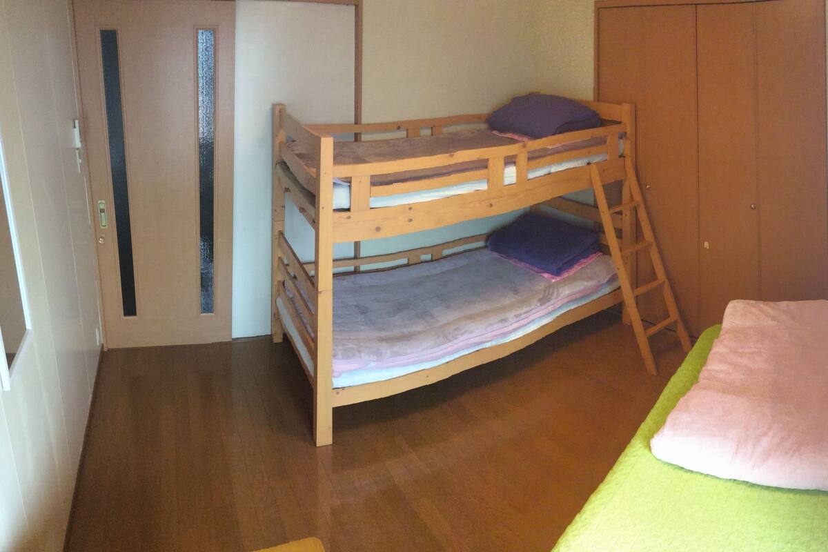 A bunk bed with a ladder, a single bed with a green mattress, and a wardrobe.