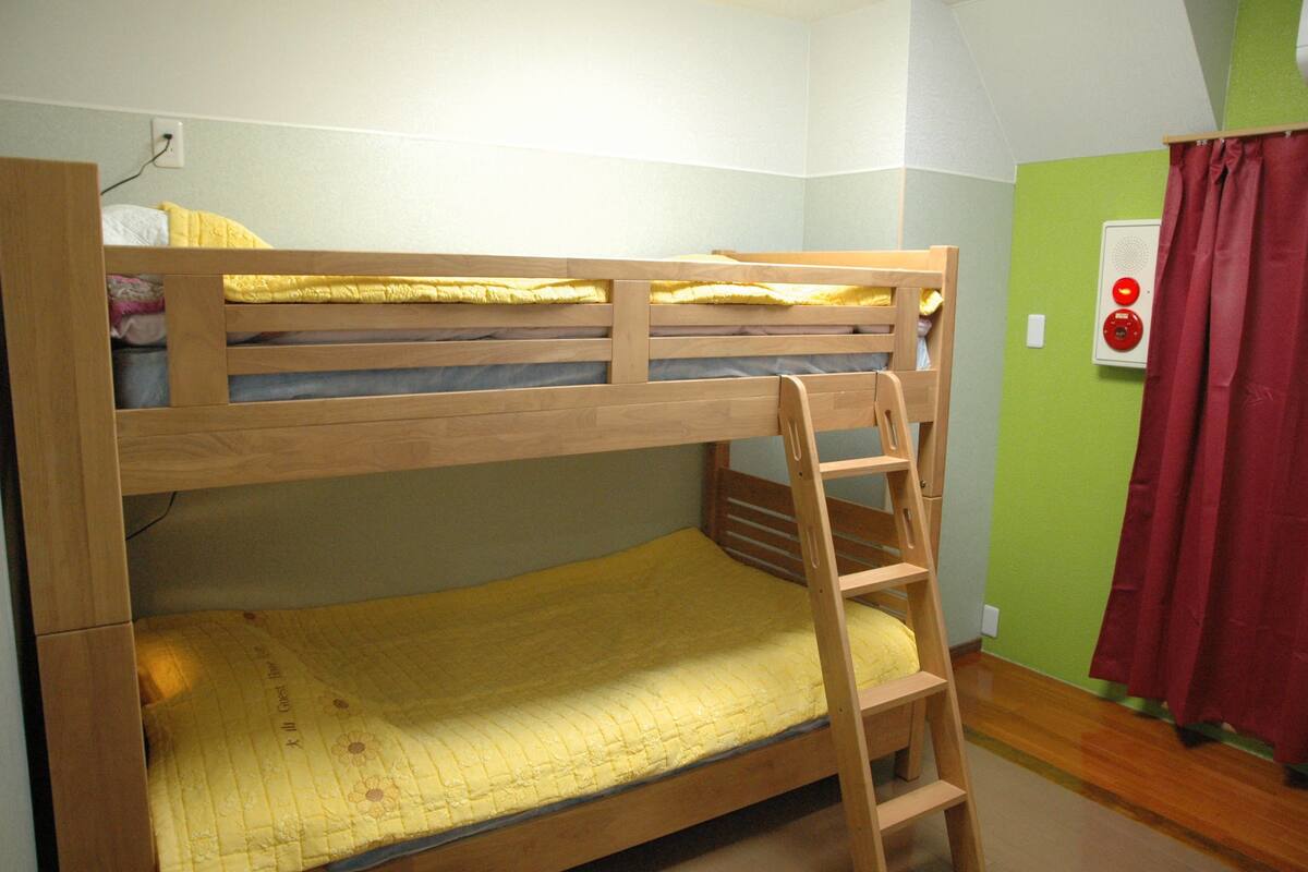 A bunk bed with a ladder, a power outlet, and a red curtain.