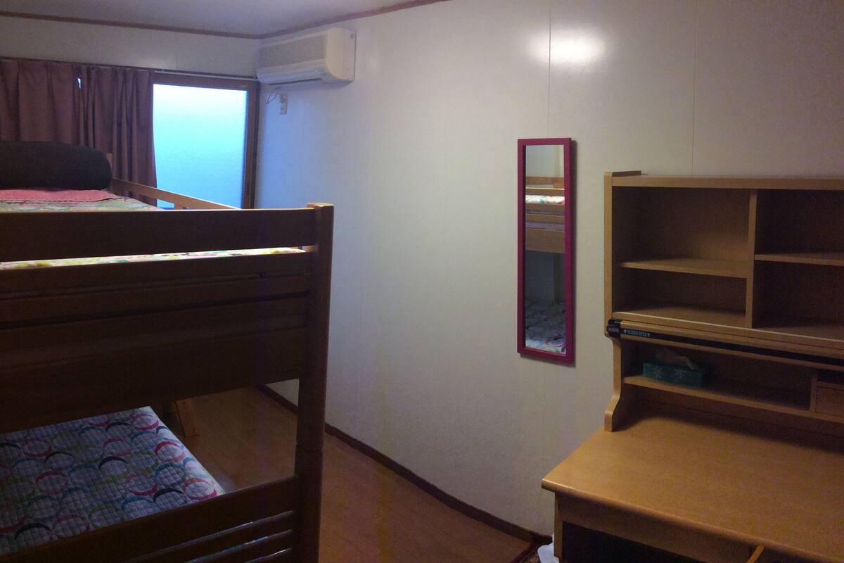 A bedroom with a bunk bed, a desk, a mirror, and an air conditioning unit.